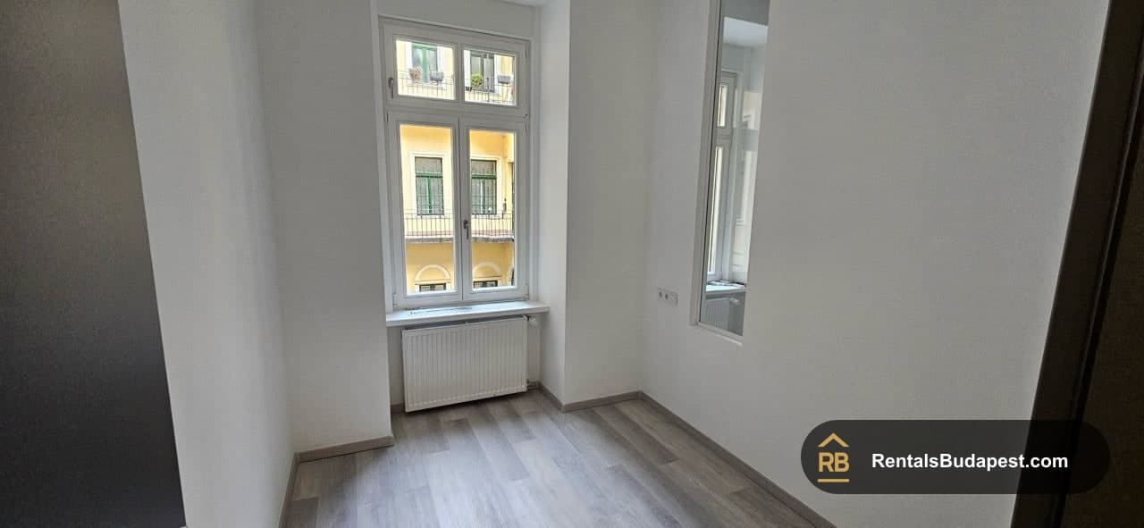Empty bedroom with grey laminate floor and window overlooking a yellow building
