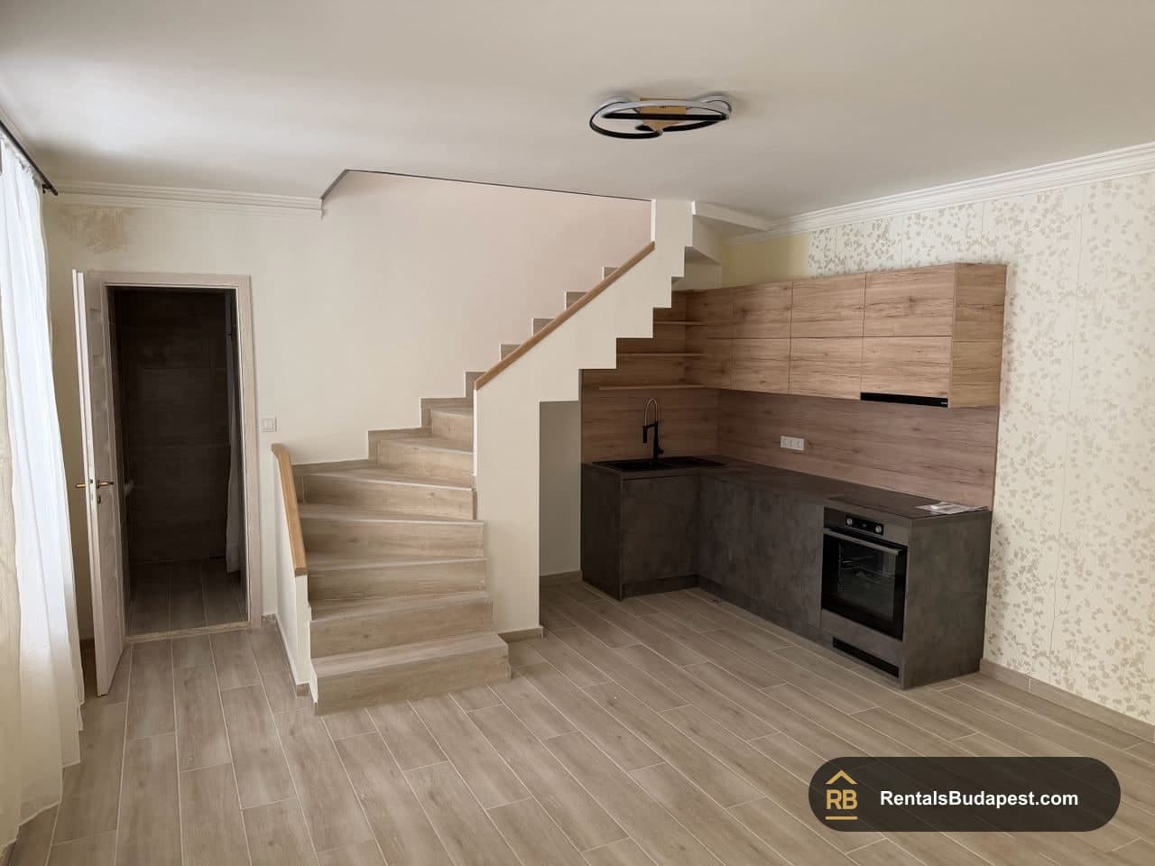 Open-plan kitchen with wood-effect cabinets, dark countertop, built-in oven and staircase to upper level, Szent István körút